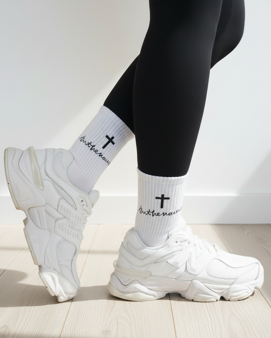 White sneakers, black leggings, and white socks with text and a cross on a light wooden floor.