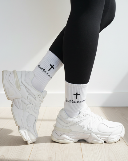 White sneakers, black leggings, and white socks with text and a cross on a light wooden floor.