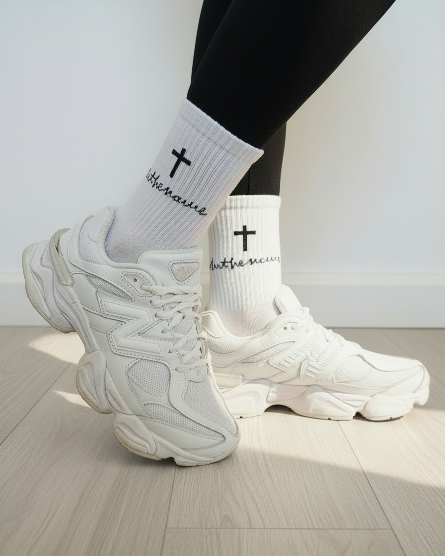 White sneakers and socks with cross designs on a light wooden floor.