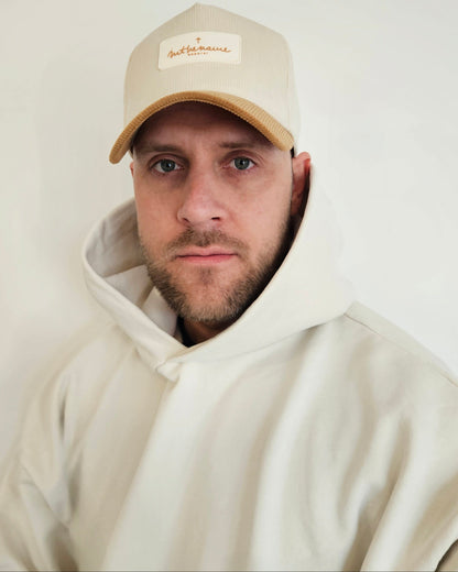 Person wearing a beige cap and hoodie with a plain background