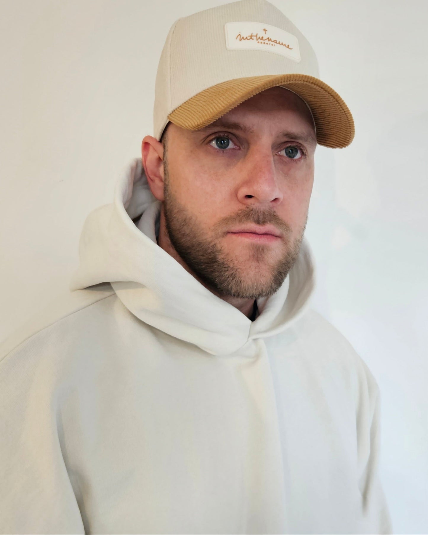 Person wearing a beige cap and light gray hoodie against a plain background